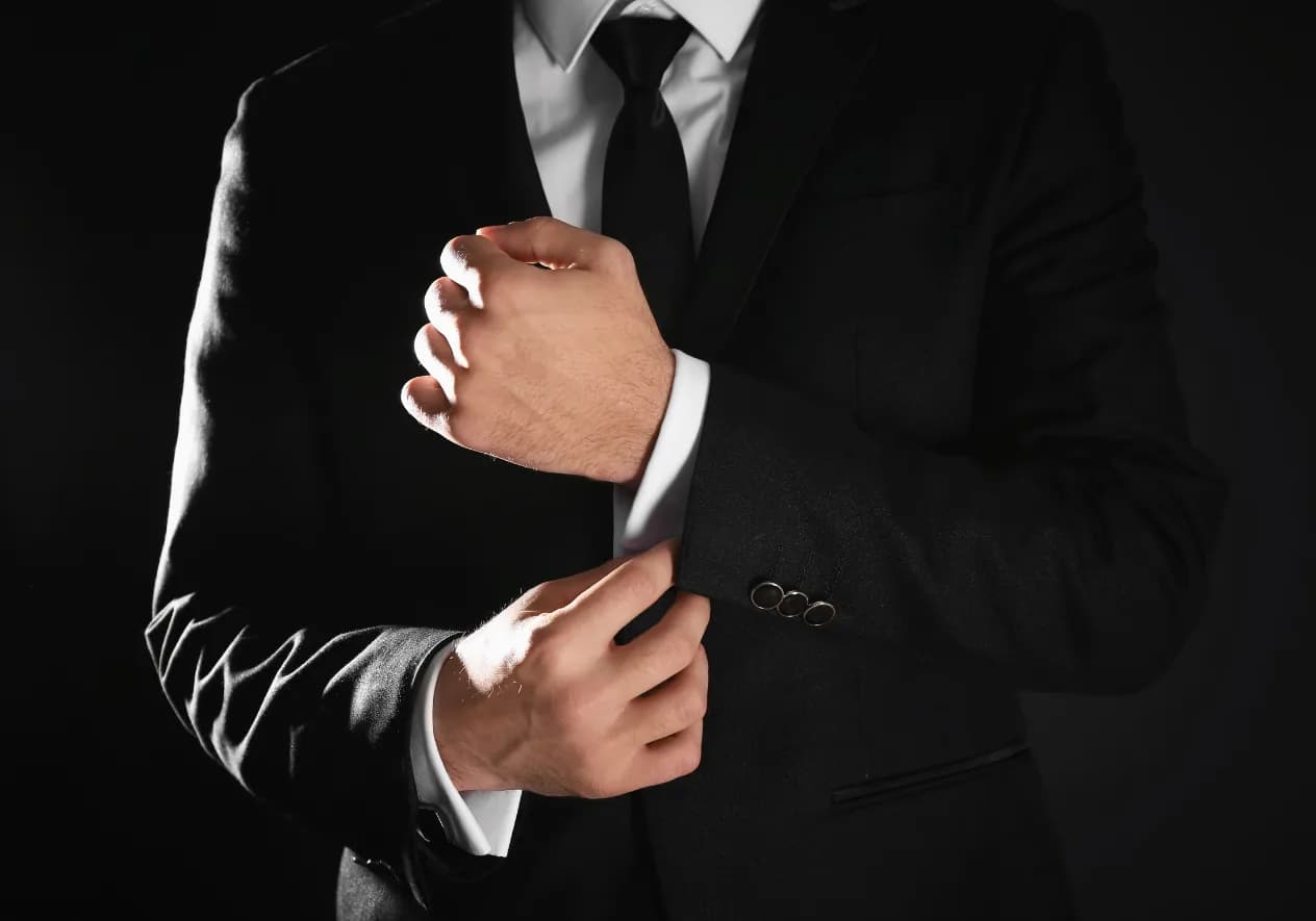 Close-up of a person in a dark business suit and tie adjusting their cuff